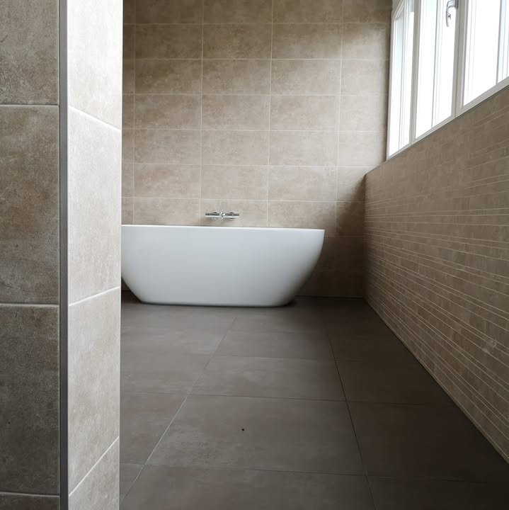 Vrijstaand bad voor een wand met beige tegels en een donkere tegelvloer
